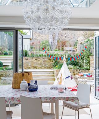 An example of kitchen extension ideas showing a dining table with a floral table cloth and white chairs in front of open glass doors