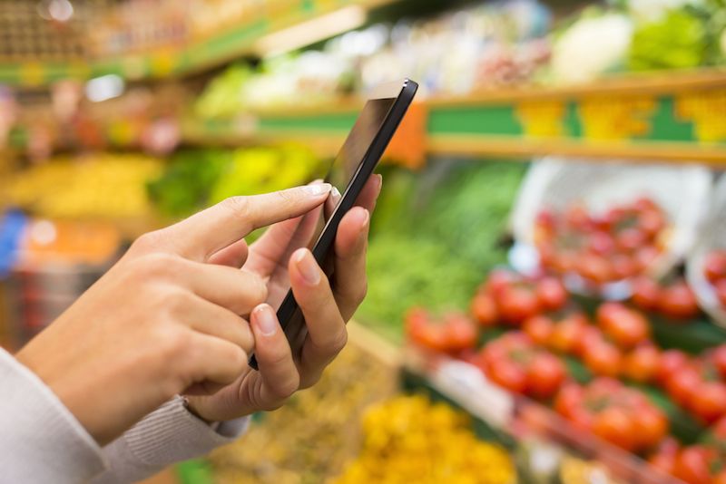 A person uses their smartphone while grocery shopping.