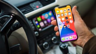 Man's hand holding iPhone in car with CarPlay screen behind