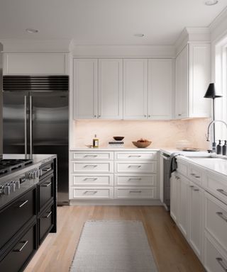 A kitchen with white cabinets, peach walls, a black hob and fridge, and a wooden floor with a white rug
