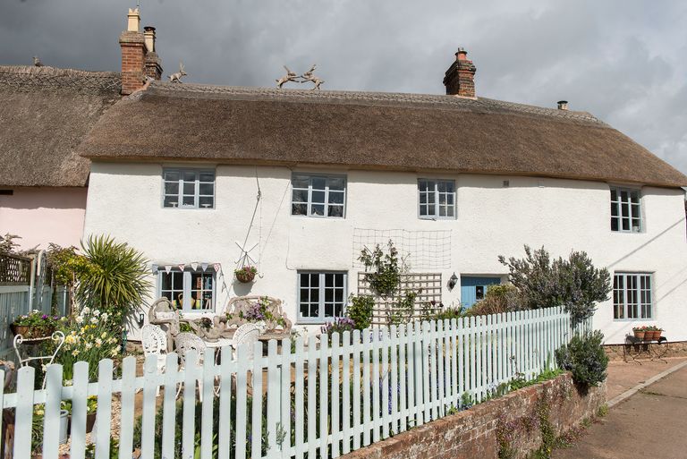 whitewashed thatched cottage exterior with blue front door and with white picket fence