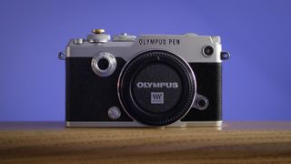 Close-up of an Olympus PEN-F camera body, against a purple background, focusing on the Creative Dial