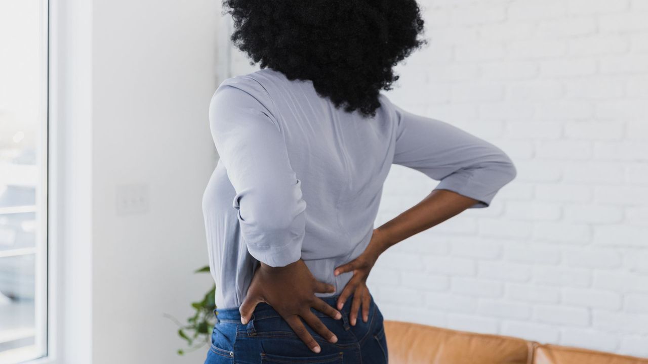 Woman wearing shirt and jeans holding onto lower back, representing the yoga stretches for lower back pain 