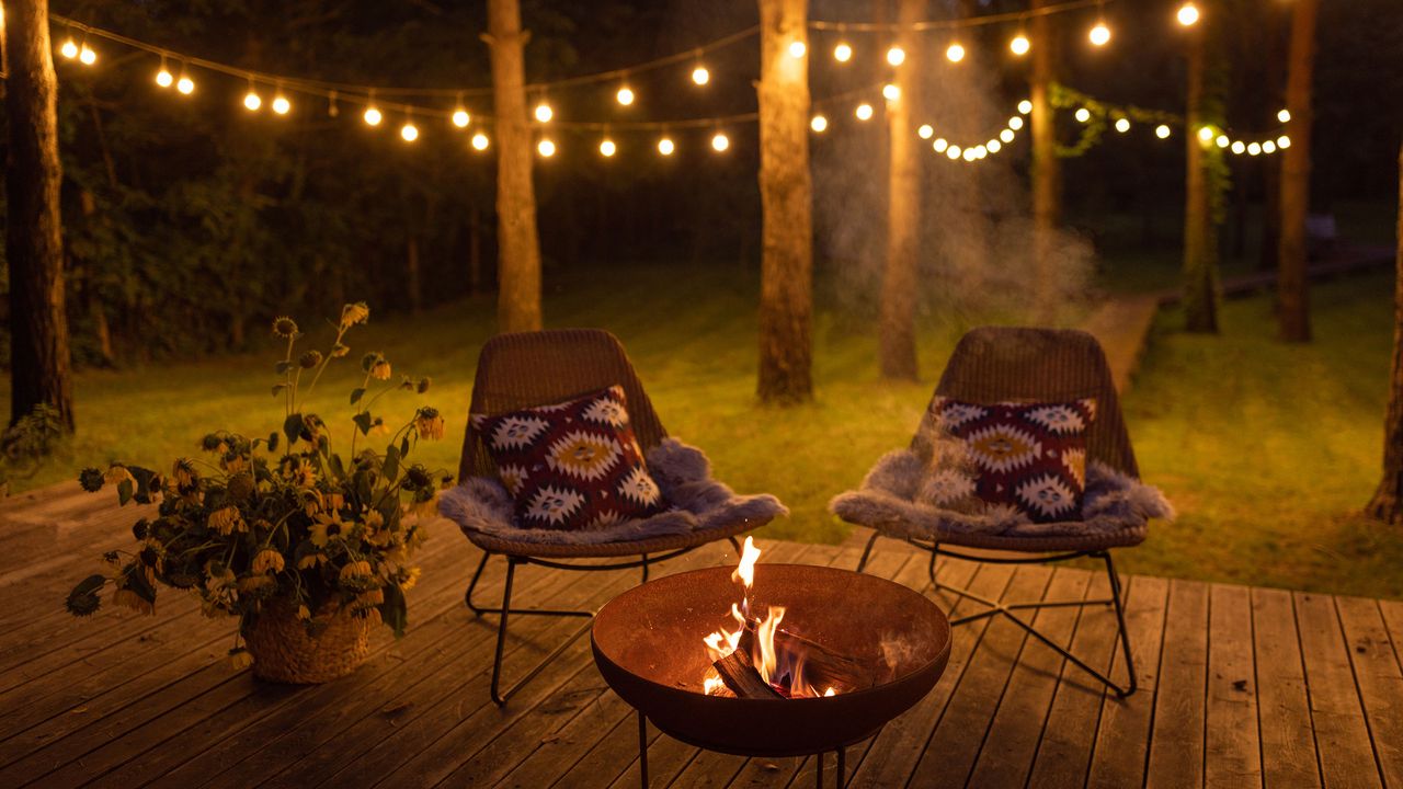 Comfortable arranged deck with fire pit and chairs. Autumn theme details. String lights in the background.