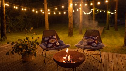 Comfortable arranged deck with fire pit and chairs. Autumn theme details. String lights in the background.