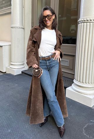 best elevated basics shown in a photo of a woman wearing a suede trench coat over a white t-shirt with blue jeans and brown ankle boots