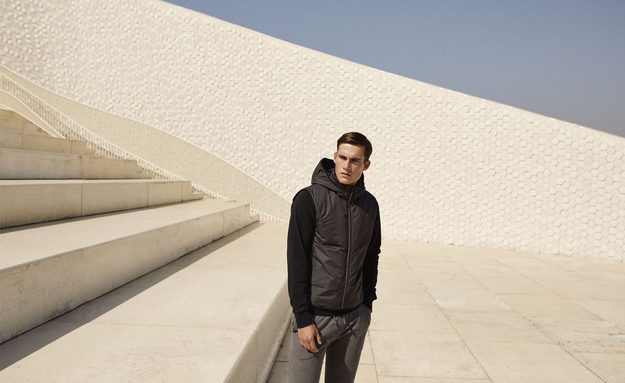 The HEDLEY Technical Hooded Vest, OWENS Pique Sweatpants, ROWE Piqué Sweater. A man standing outside at the bottom of a staircase wearing casual clothing.