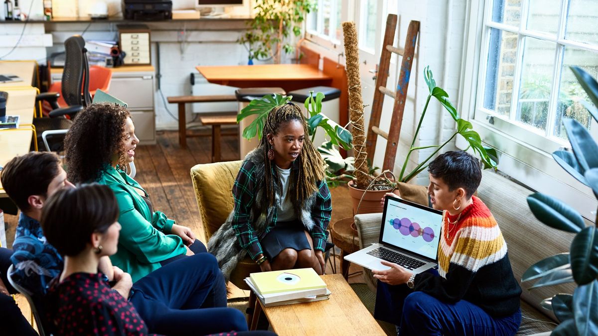 A group of diverse young workers sitting at couches in their office in a huddle, having a discussion