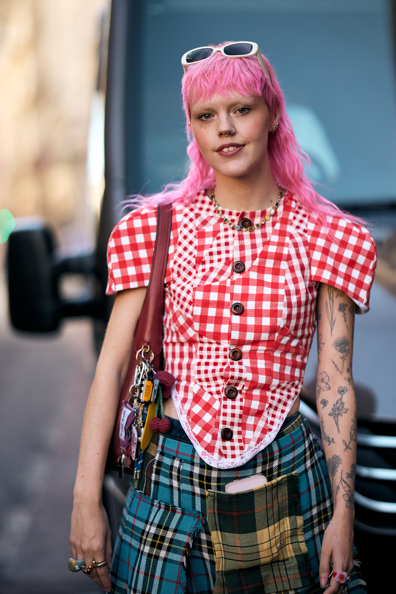 a white woman with pink hair and bangs in a gingham shirt and plaid skirt