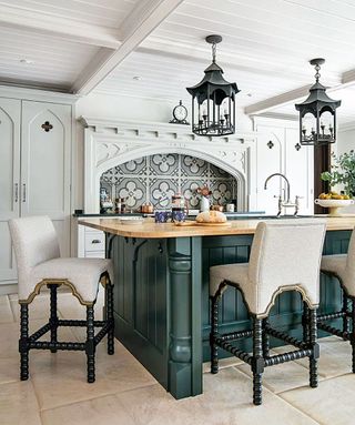 A dark green kitchen island in a gothic-inspired scheme with black pendant lights and pale gray painted units.