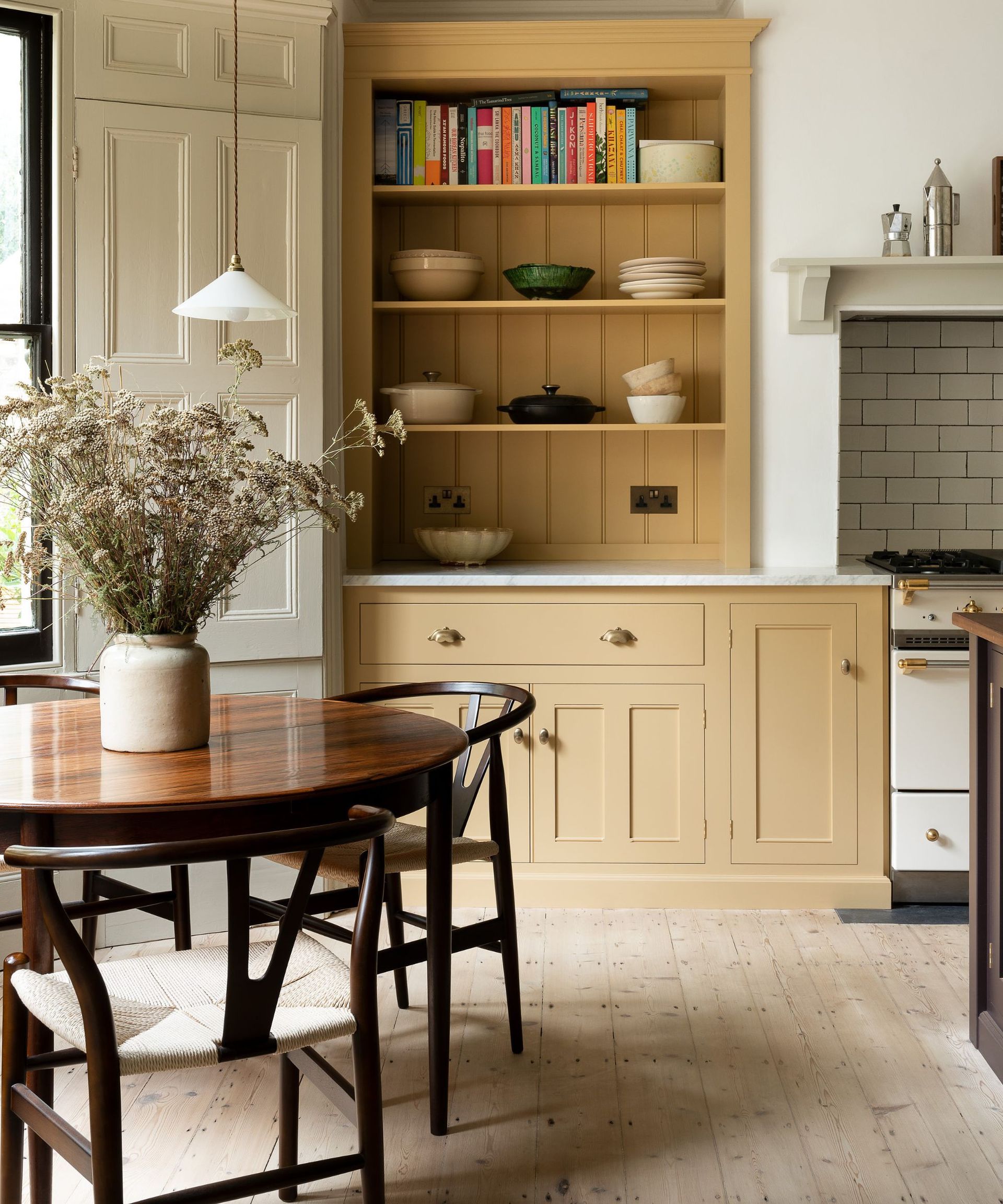 yellow shaker kitchen with a wooden round table and chairs with a large vase of flowers at its center