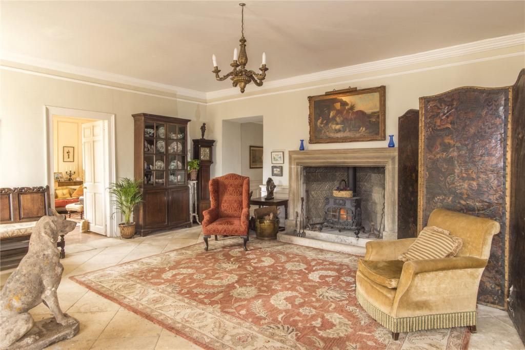 The living room of the house with grandfather clock an open fireplace, armchairs and a large red rug