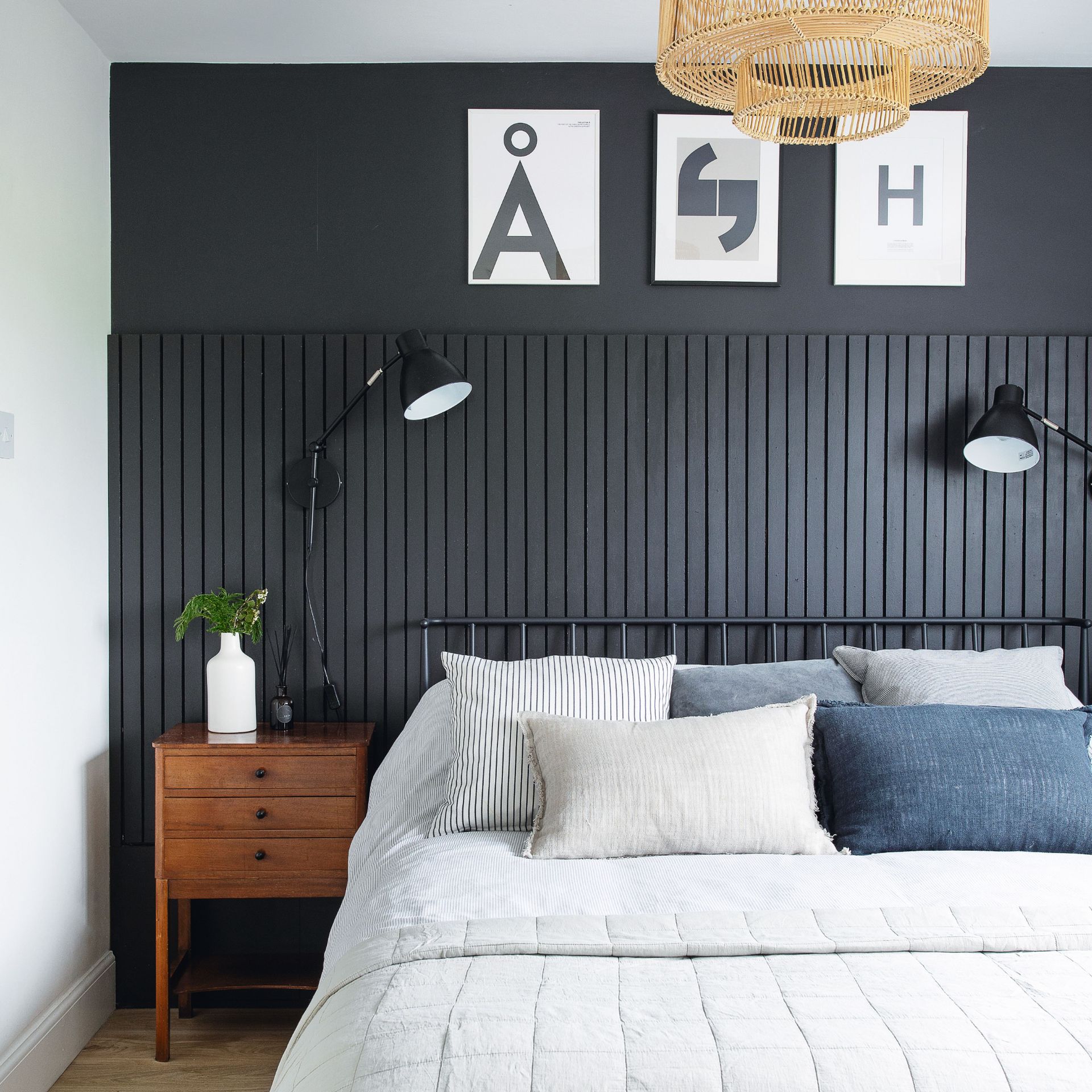 Bedroom with navy blue panelled feature wall, bed with blue decorative cushions, and wooden dresser table