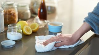 woman cleaning kitchen countertop with baking soda and lemon in the background