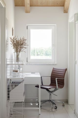 white office in a hallway next to a window, with a brown leather office chair