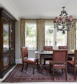 Traditional dining room with deep red carpet, chair cushions and lampshades and dark wood cabinet and dining table