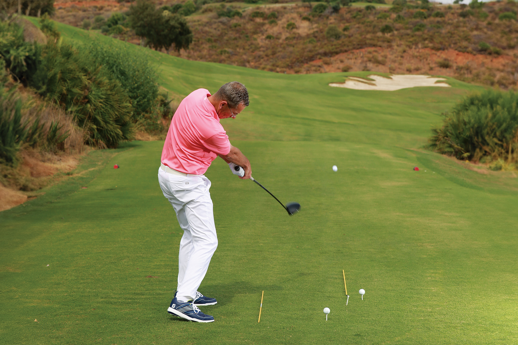 A demonstration of a drill to cure a hook, with three tee pegs on the ground in a curved shape, and two alignment sticks on the ground