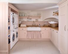 Pink laundry room with sink, cupboards, washer and dryer, door curtain, basket on countertops, hangers, white painted ceiling