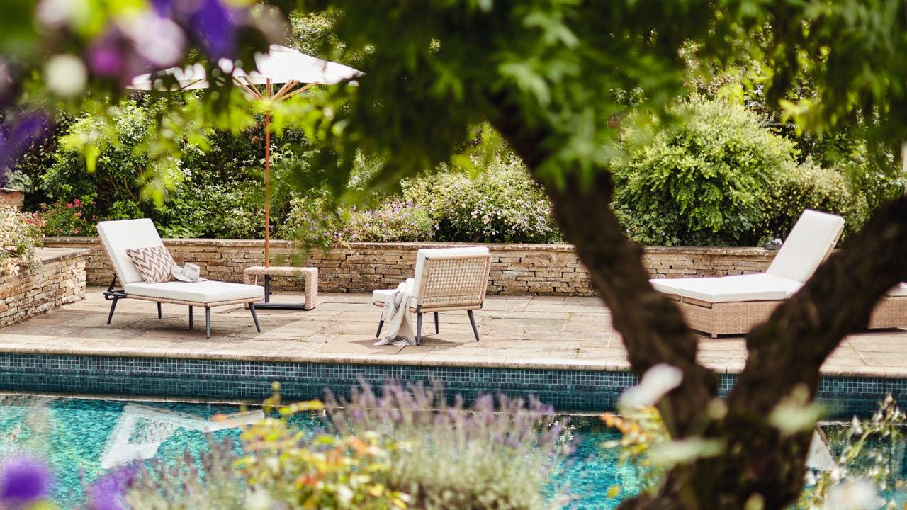 A group of sun loungers by the side of a garden pool