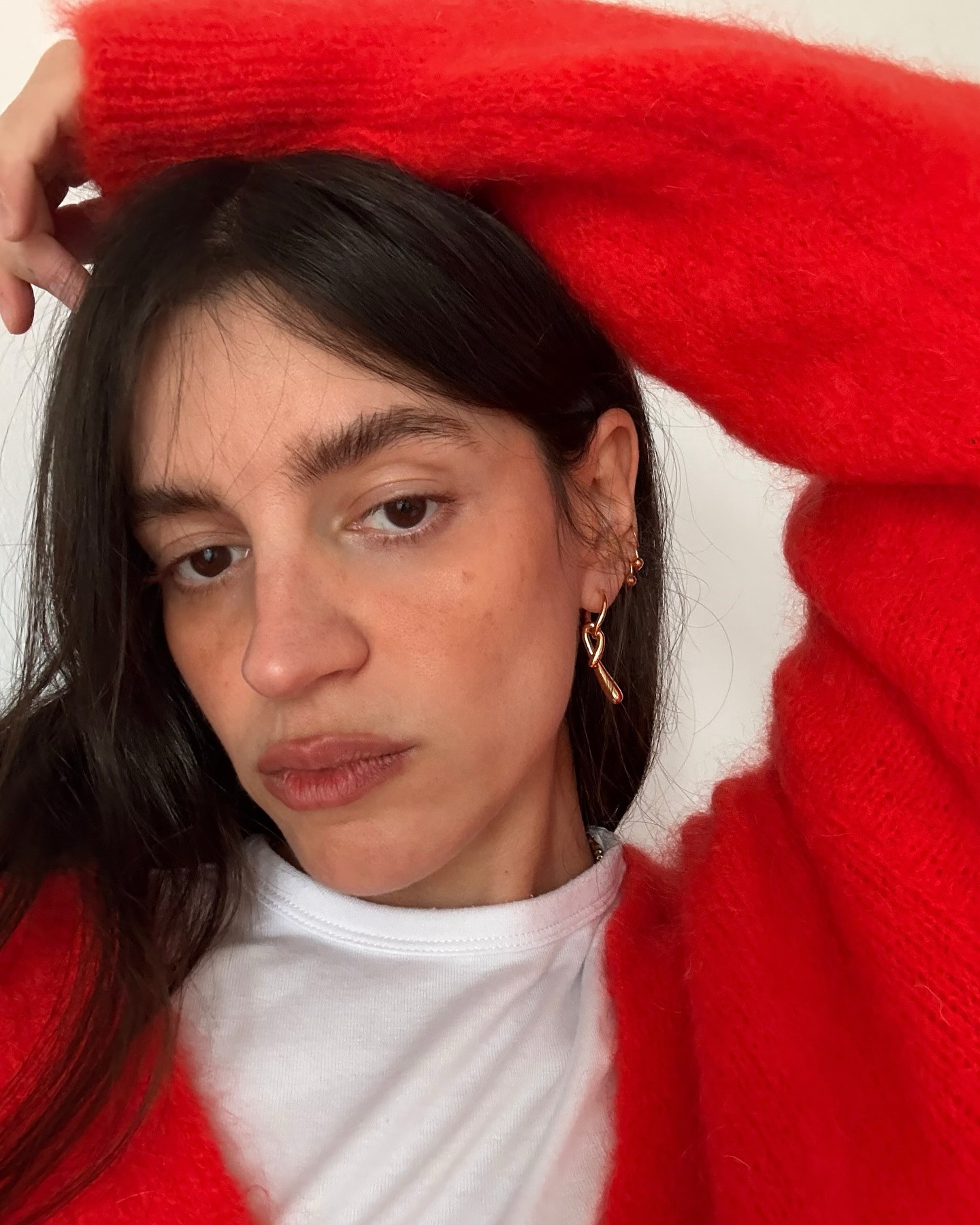 A woman wearing a red sweater over a white t-shirt and multiple earrings