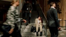Frustrated woman in a business suit sitting on stairs while other workers walk around her in a blur 
