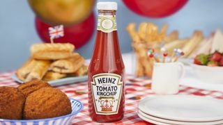 A bottle of Heinz Kingchup on a check tablecloth with buffet food in the background