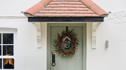 A sage green front door with a berry-encrusted Christmas wreath on it