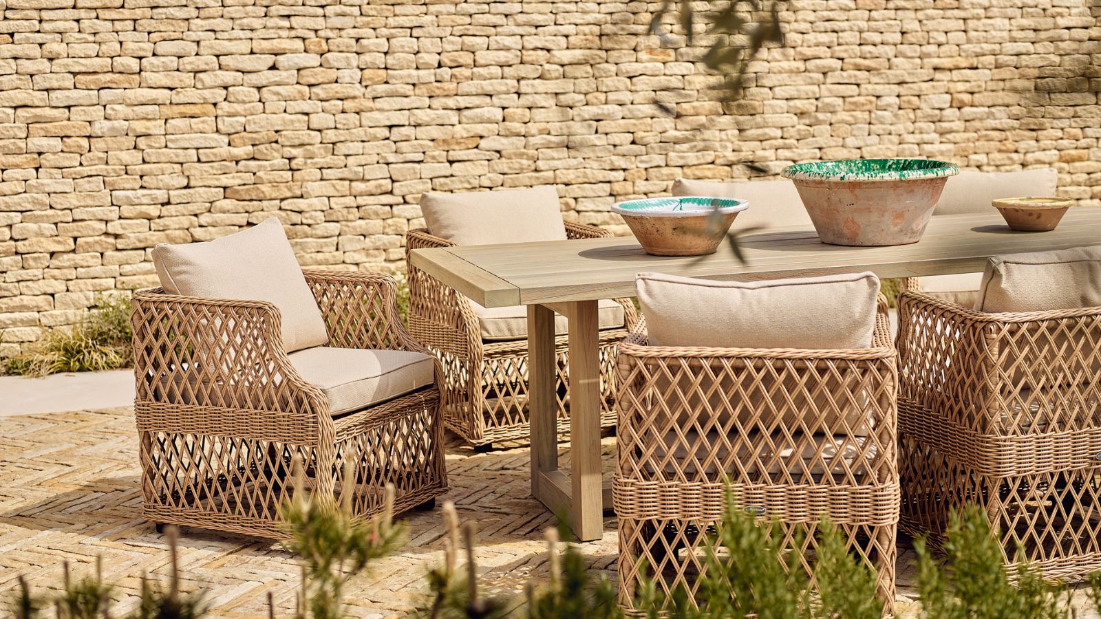 Woven wicker patio chairs around an outdoor table, on a brick patio. 
