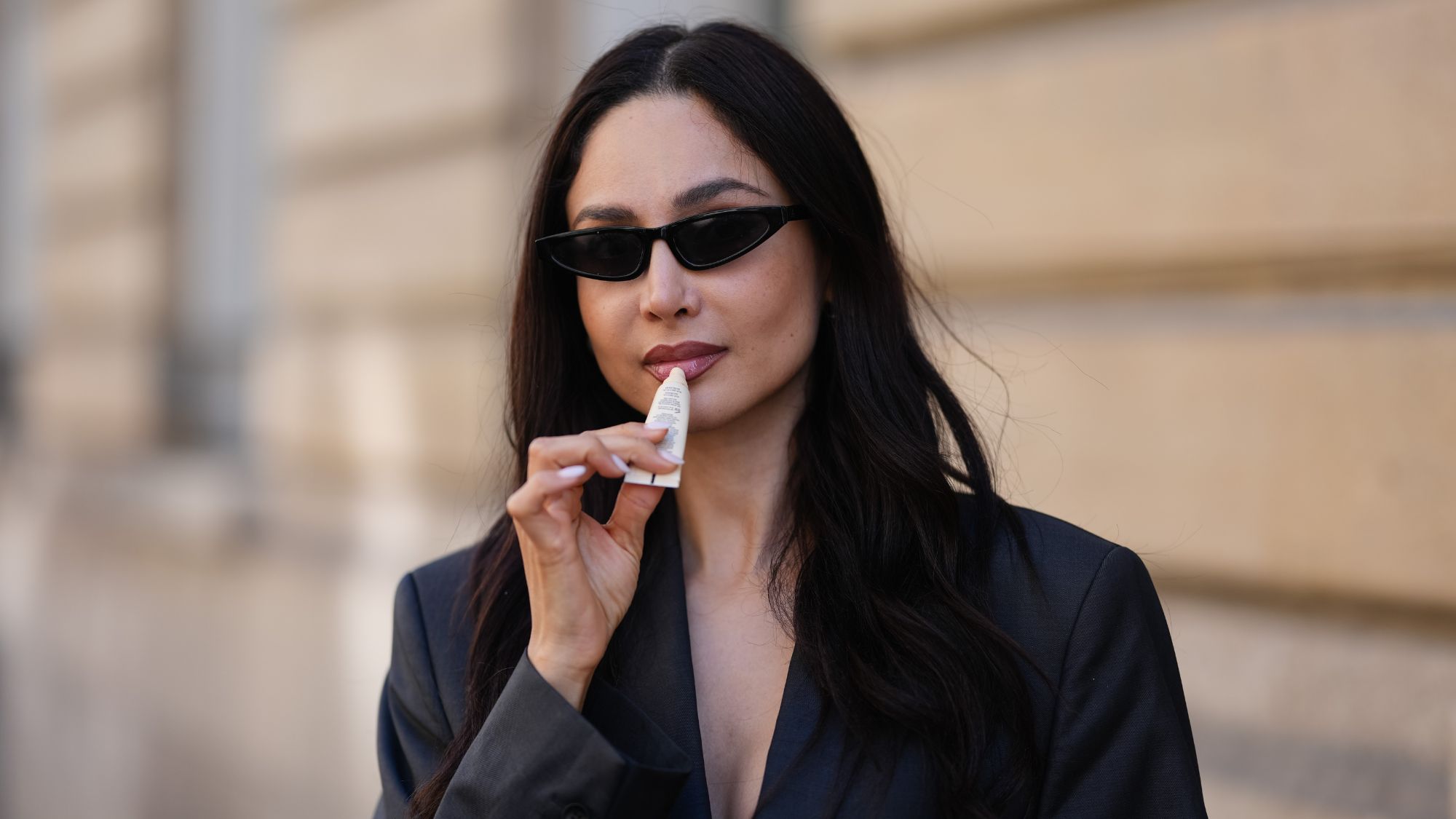 street style shot of woman in sunglasses applying lip balm