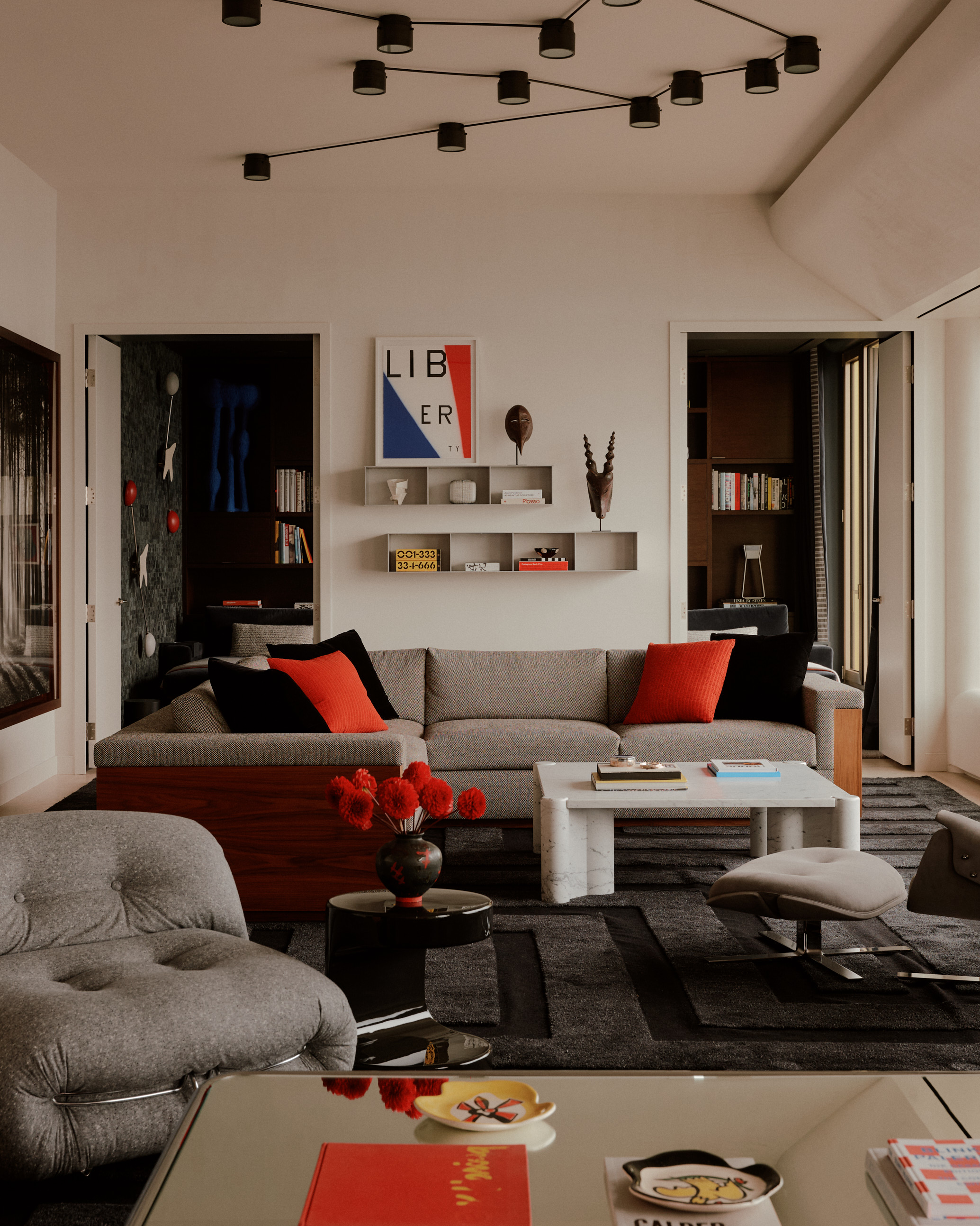 modern living room with primary color palette, gray sofa, red cushions, gray armchair, mirrored coffee table, wall shelfs, pendant light
