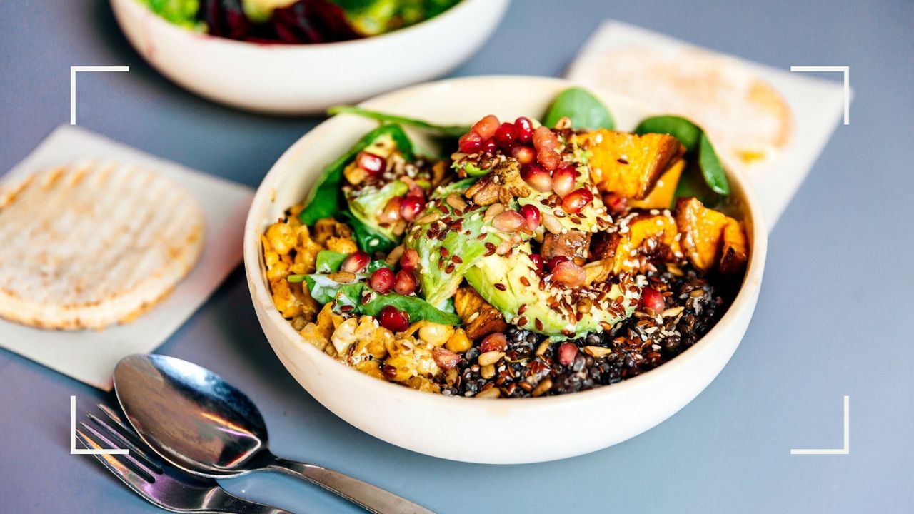 Plate of salad, grains and pomegranate seeds in white enamel bowl on table