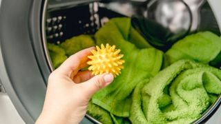 A rubber yellow dryer ball being added to a clothes dryer filled with green towels