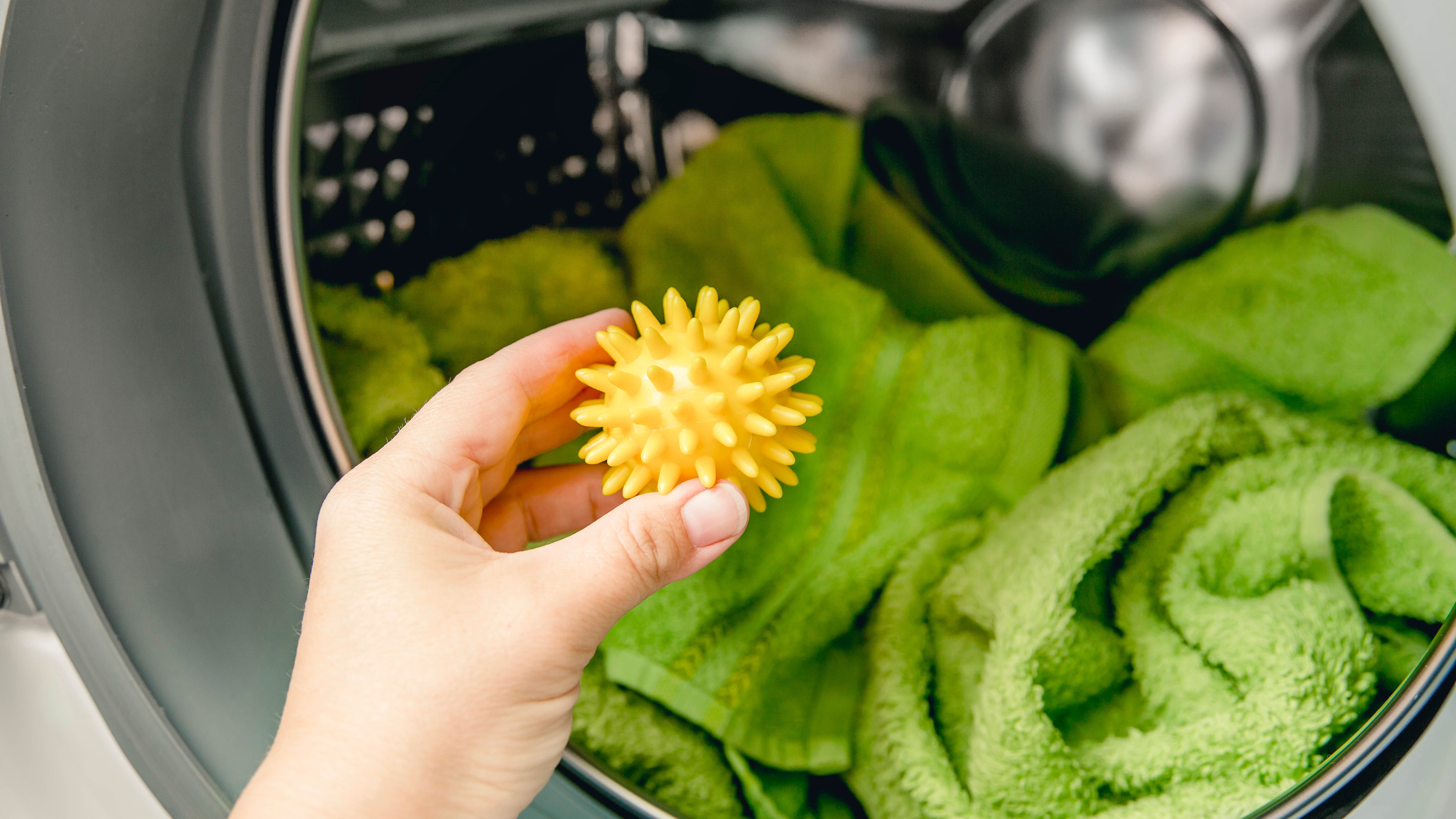 Резиновый желтый шарик для сушилки добавляется в сушилку для белья, наполненную зелеными полотенцами.