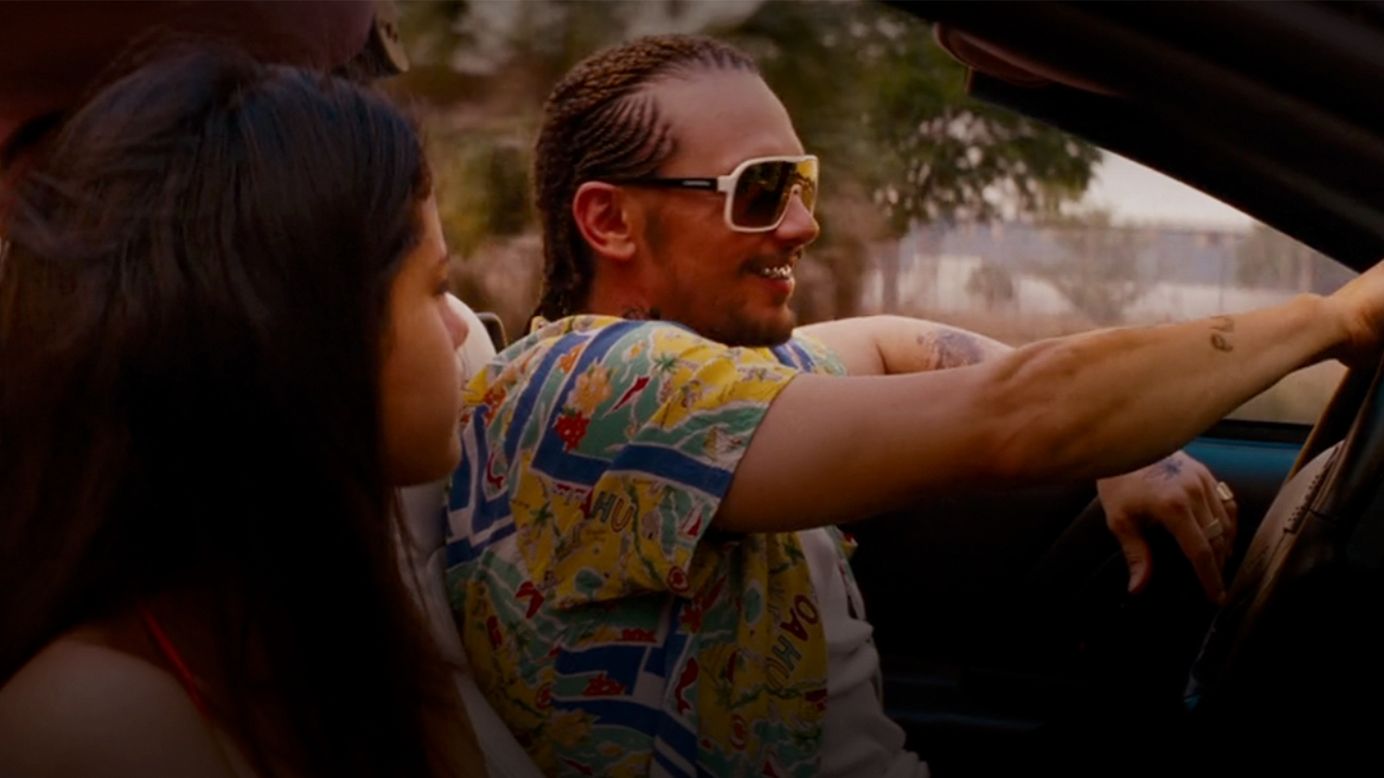 A woman riding shotgun in a car with a man wearing sunglasses and driving