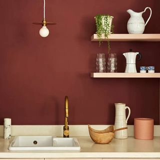 kitchen with terracotta red walls, cream worktop and wooden shelves