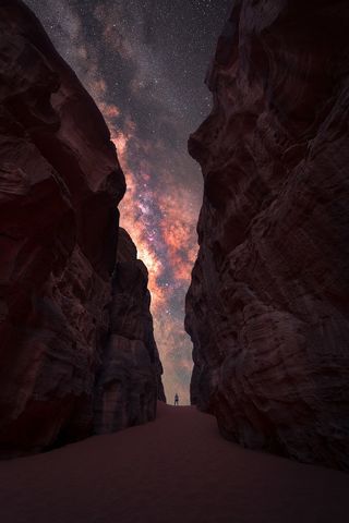 Milky way photographed between two tall cliffs with a lone man standing in the center