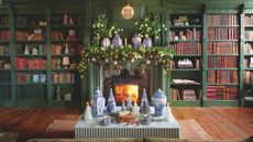 A living room with green built-in shelving, filled with books and Christmas decor, surrounding a lit fireplace with a garland hanging over the mantel 