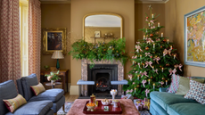 Yellow living room decorated for Christmas with a garland over the mantel and a tree decorated with candles and bows