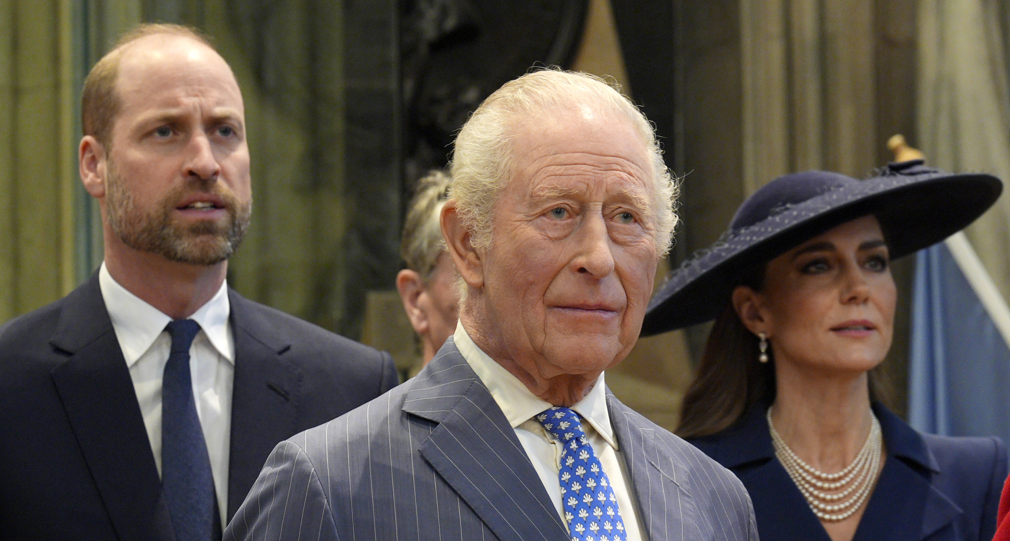 King Charles standing in front of Prince William, both wearing suits and ties
