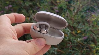 The Shokz OpenDots One in front of a green bush.