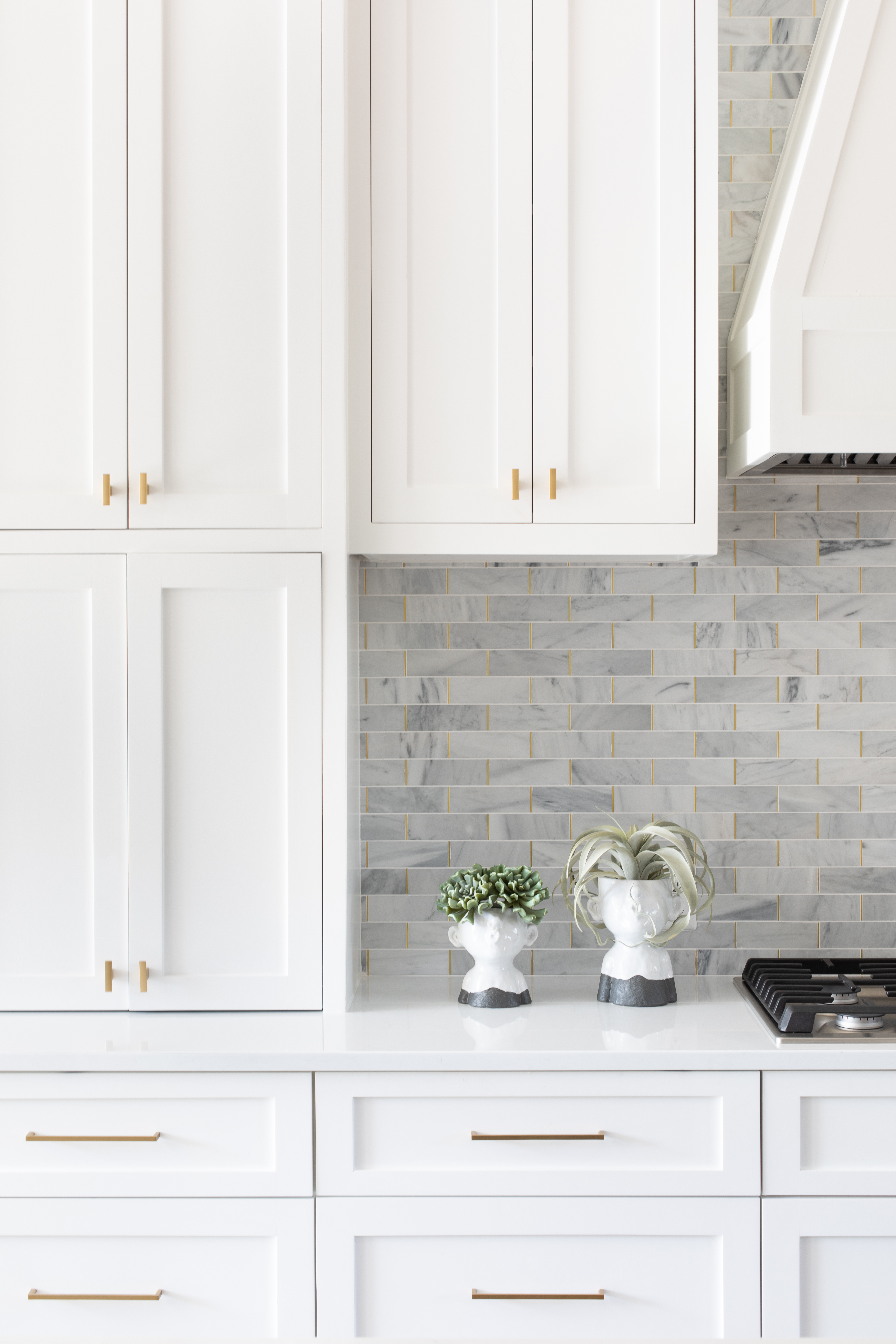 A white kitchen with white cabinets, gold pull bar handles, and grey subway tiles