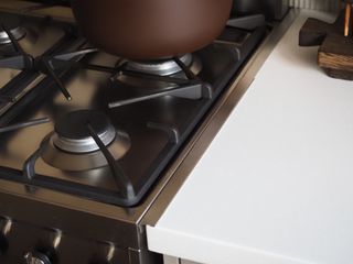 a oven gap filler on a stainless steel stove next to a brown pot with a marble oval board