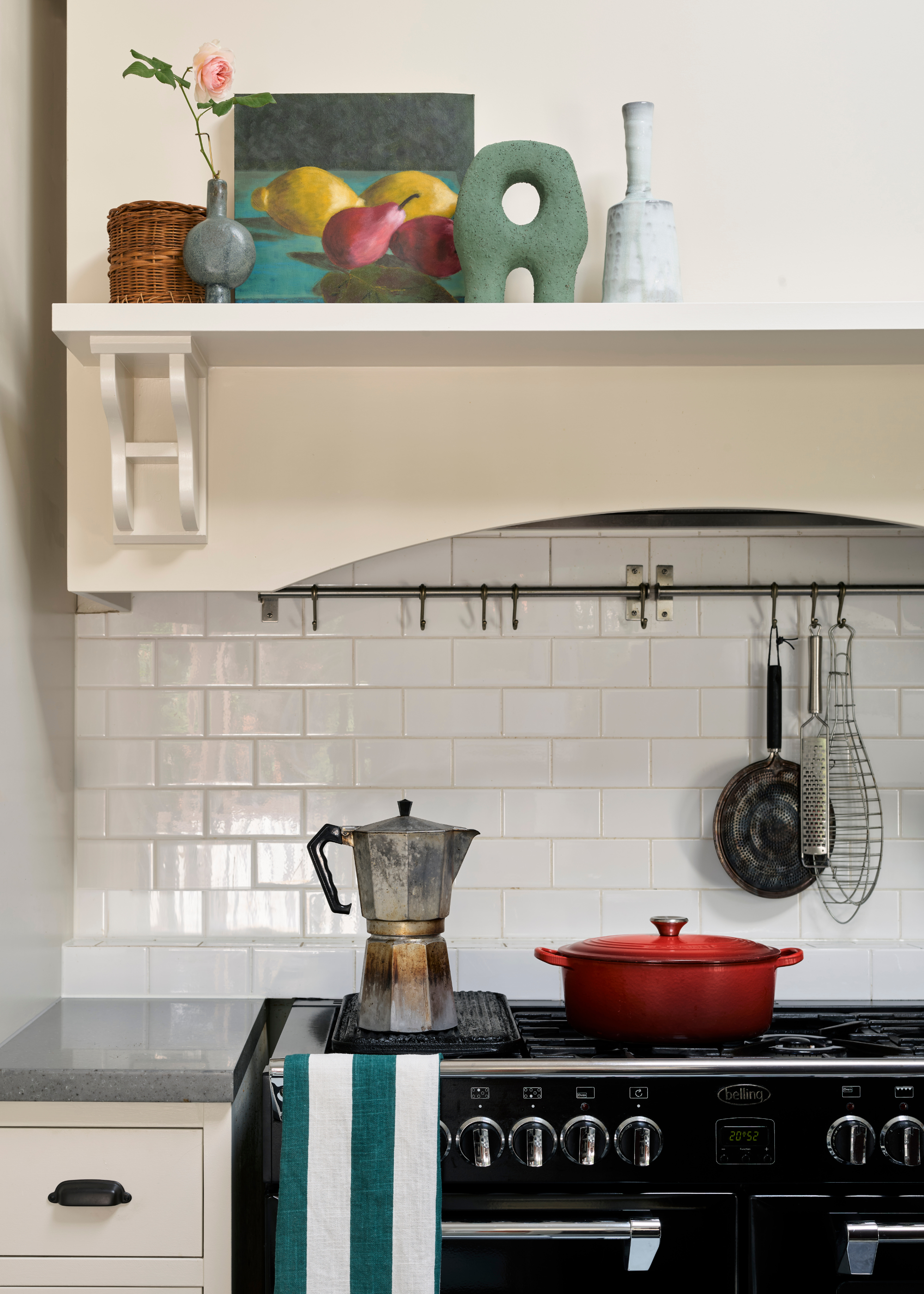 A close-up of a stove area with a moka pot, a Dutch oven, and a hanging rail