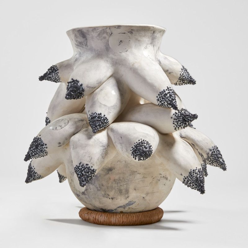 A porcelain sculpture echoes female breasts in white- and black-toned shapes, all positioned on a wicker base.
