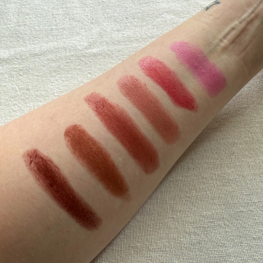 Close up shot of the inside of a forearm with swatches of six shades of the Haus Labs Glassy Blush Balm Sticks