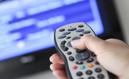 Close up of hand holding a Sky remote control pointed at TV