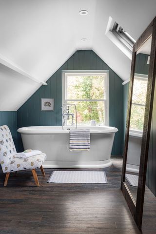 attic bathroom with blue walls and freestanding white tub large mirror and statement chair