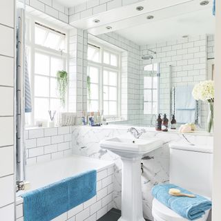 bathroom with white metro and marble effect tiles slate floor tiles white toilet and pedestal basin large wall mirror and bright blue towels