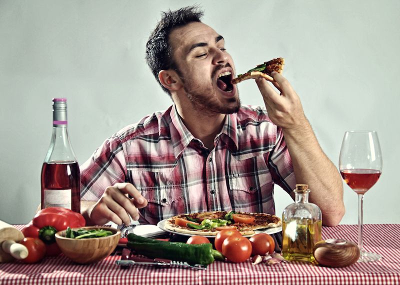 Man eating a whole pizza with wine.