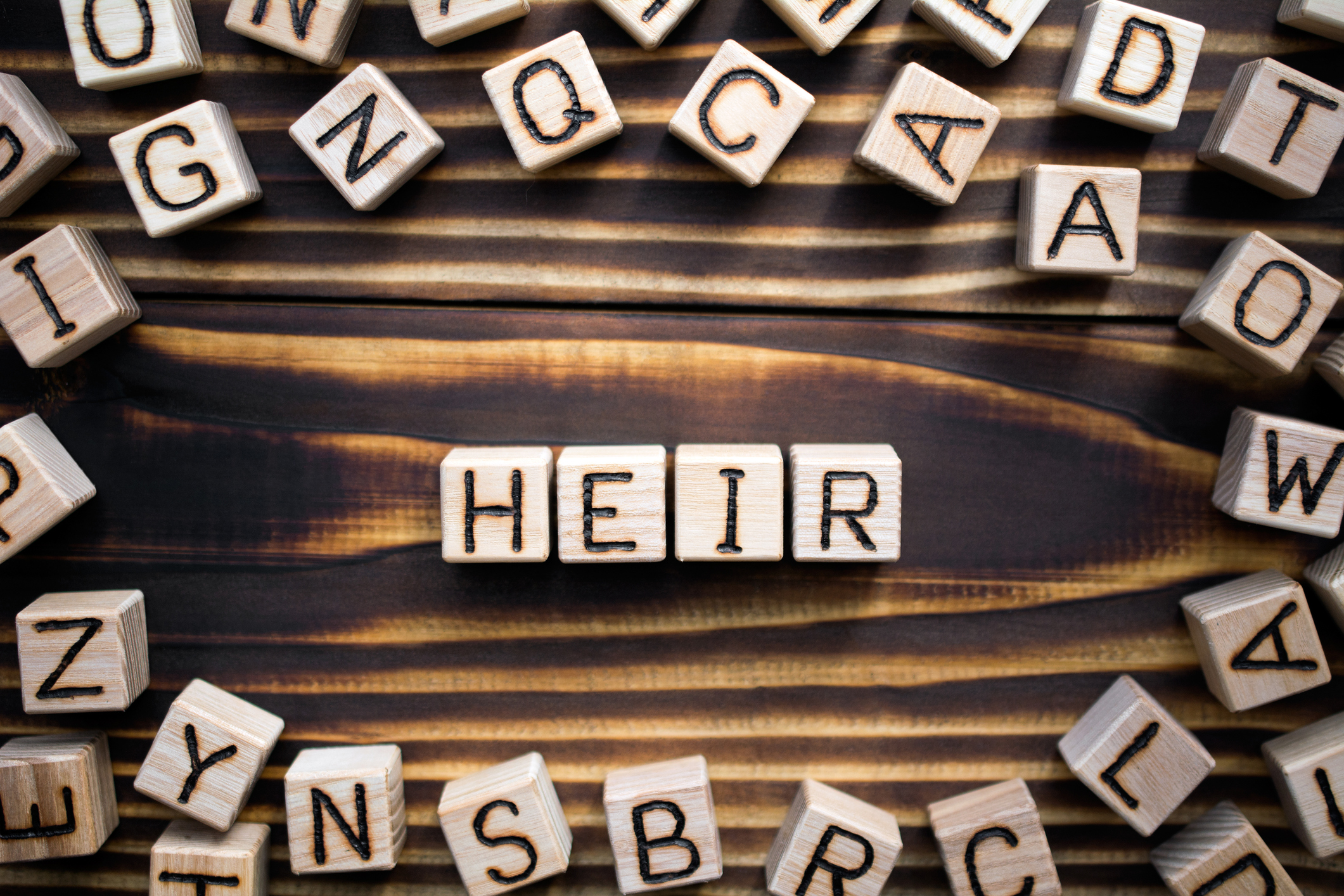 word heir composed of wooden cubes with letters, with random letters scattered around, top view on wooden background